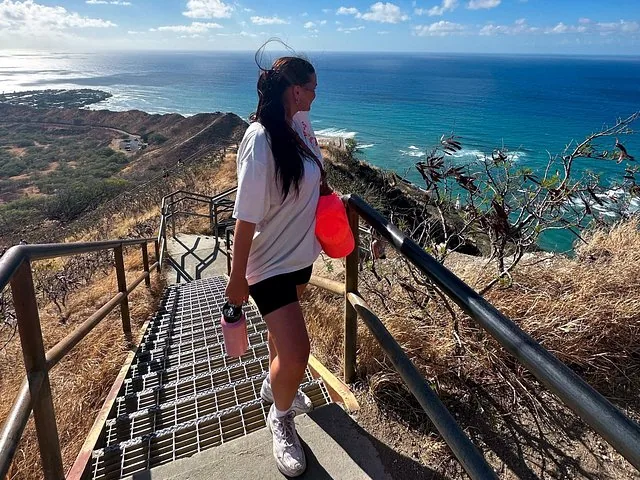 A woman walks down stairs on a hillside with ocean views.