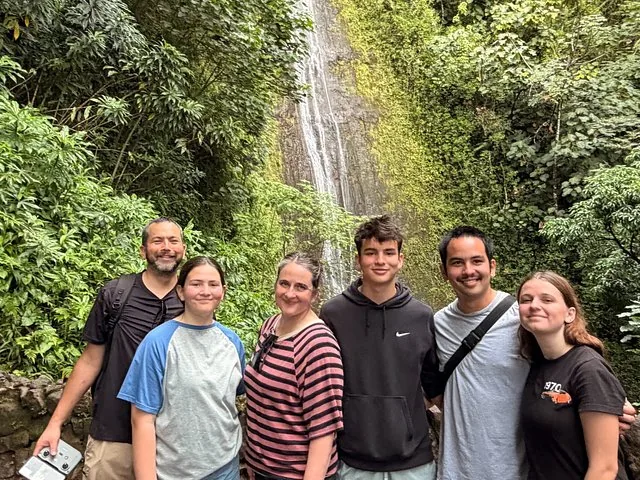 Group of six people smiling in front of Manoa Falls surrounded by lush greenery