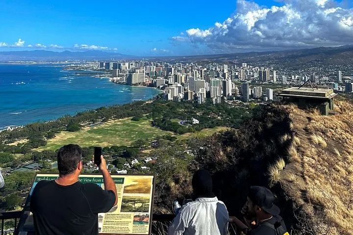 Des personnes admirant les gratte-ciel de la ville et l’océan depuis un point de vue en montagne.